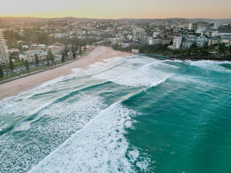 Aerial drone view of beautiful Manly Beach with foamy waves rolling and crashing at sunset